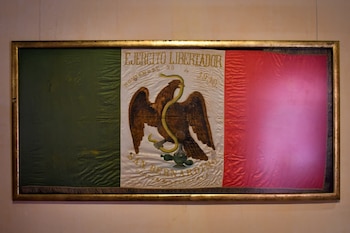 Bandera histórica mexicana enmarcada, con franjas verticales verde, blanca y roja. En la franja blanca, un águila con una serpiente y texto antiguo
