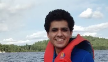 Un hombre joven sonriente con chaleco salvavidas rojo y camiseta azul sobre un cuerpo de agua rodeado de árboles y vegetación