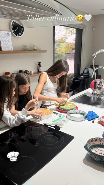 Tres niñas decoran pasteles sobre una mesada blanca en una cocina iluminada con moldes y utensilios de repostero