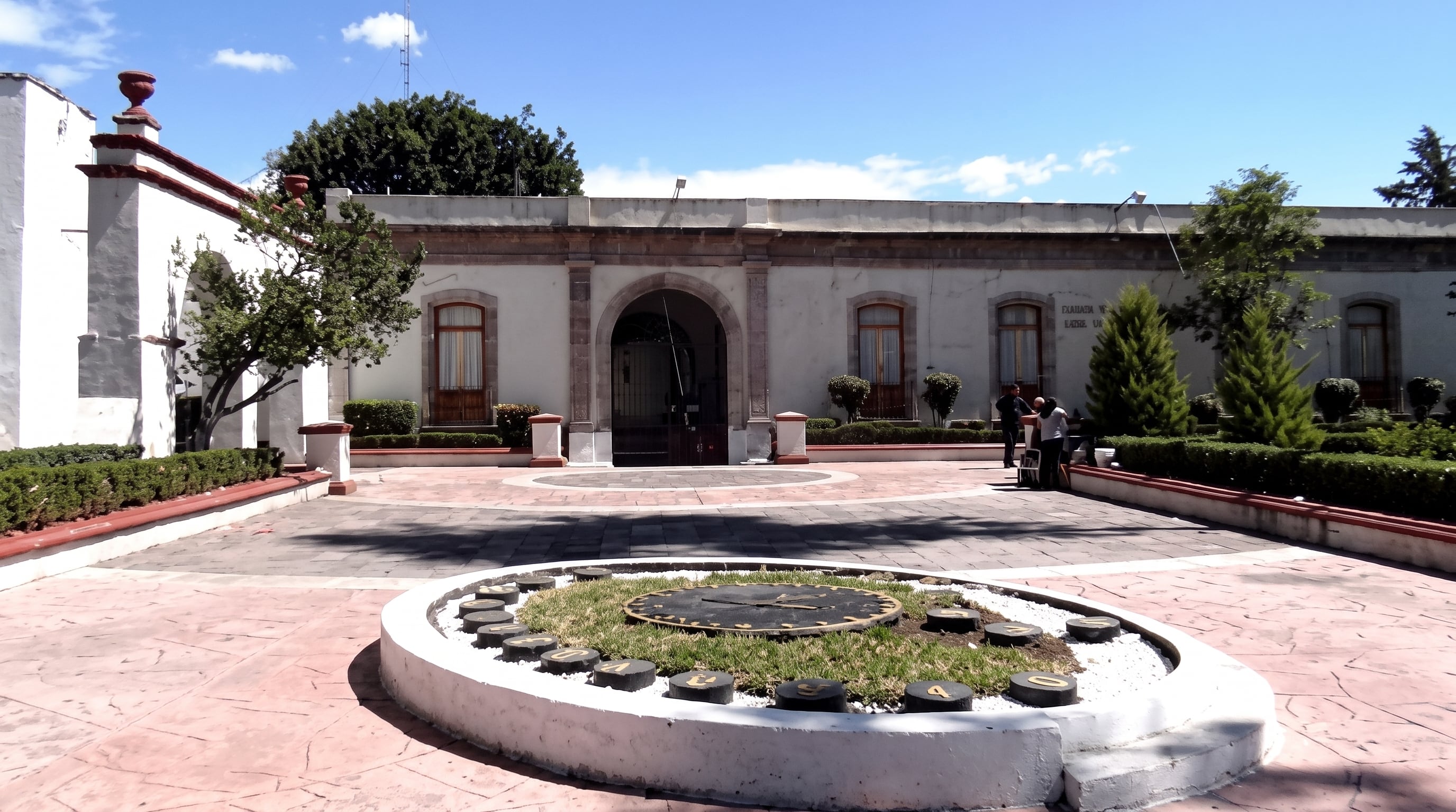 Un patio central pavimentado alberga un reloj de suelo en primer plano ante la fachada de un edificio histórico con arcos de piedra y ventanas. (Archivo Gobierno México)