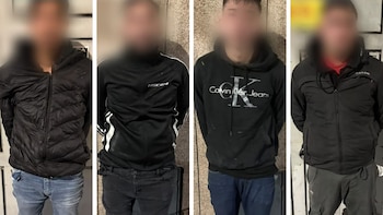 Cuatro hombres con rostros pixelados y vestimenta casual oscura, de pie, fotografiados en un interior con pared clara