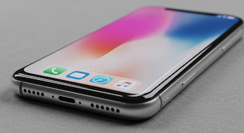 Primer plano de un prototipo de iPhone plateado en una superficie gris, con pantalla encendida mostrando íconos y bordes curvos en sus cuatro lados.