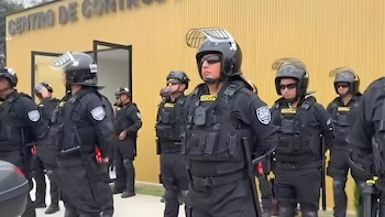 Agentes de seguridad con cascos, chalecos tácticos y uniformes negros en formación frente a una estructura de color amarillo