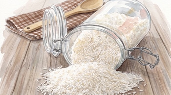 Un frasco de vidrio tumbado con arroz blanco derramado sobre una mesa de madera, una cuchara de madera y un paño a cuadros.