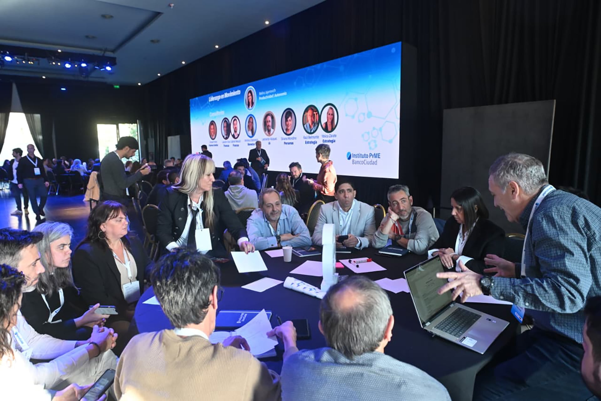Varios asistentes conversan y trabajan en mesas redondas durante un seminario de capacitación del Ciudad y el Ministerio de Desarrollo Económico porteño