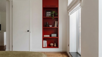 Interior moderno do quarto. Uma estante vermelha brilhante pode ser encontrada em uma parede branca, com livros, plantas e objetos. Existem janelas e portas.
