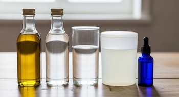 Cinco recipientes de vidrio y plástico con líquidos transparentes, amarillos y blancos, además de una pequeña botella azul con gotero, sobre una mesa de madera.