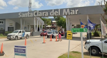 Arco de acceso con las letras Santa Clara del Mar, dos patrulleros policiales, conos naranjas y automóviles sobre la calle