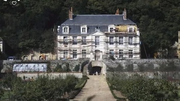 Château La Fourchette, un edificio de piedra con tejado oscuro, cubierto parcialmente por andamios. Un sendero de jardín conduce a la entrada. Fondo de árboles frondosos