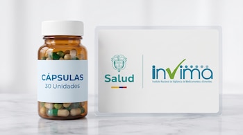 Un frasco de vidrio ámbar con cápsulas verdes y beige junto a una placa con los logotipos de Salud y del Invima sobre una mesa.