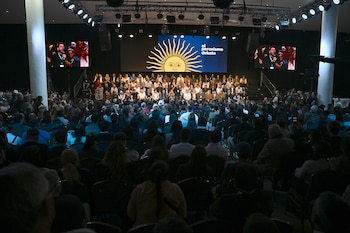 Vista general de un auditorio lleno de gente sentada frente a un escenario con una gran pantalla que muestra un sol amarillo y el texto "el peronismo debate"