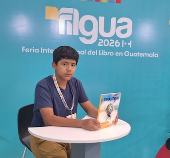 Joven con camiseta azul y cordón en el cuello sentado en una mesa blanca, sostiene un libro. Fondo azul con texto "filgua 2026 Feria Internacional del Libro en Guatemala"