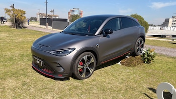 Un automóvil de color gris oscuro mate con detalles rojos estacionado sobre césped en un área al aire libre