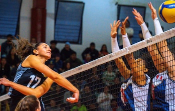 Una jugadora de voleibol con la camiseta número 17 salta para golpear el balón sobre la red frente al bloqueo de dos contrincantes