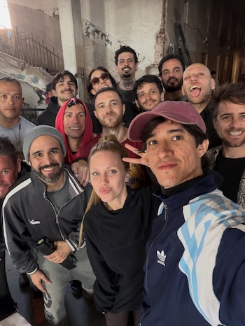 Un grupo de catorce personas posa para una fotografía estilo selfie en un salón con muros descascarados