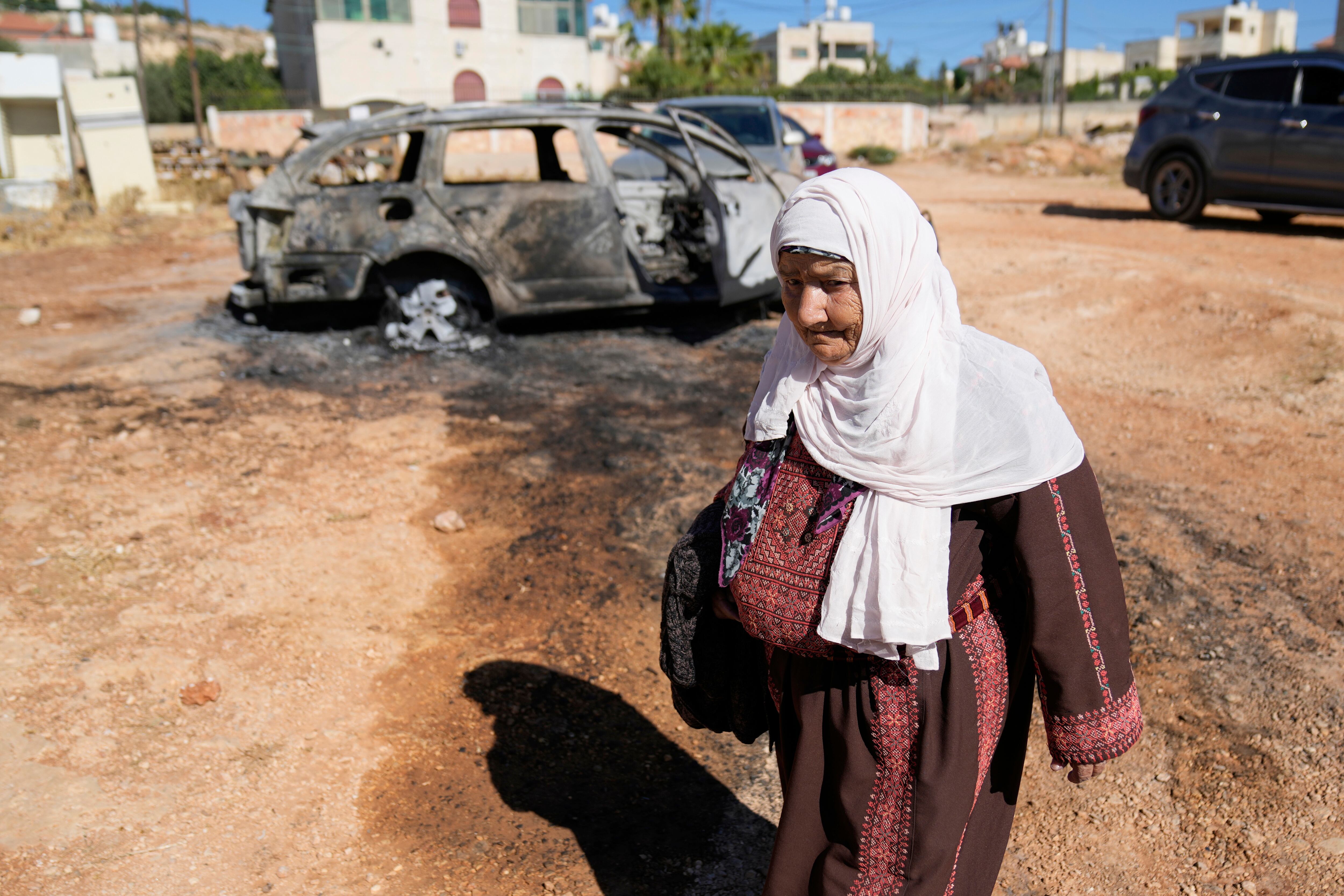 Una mujer camina frente a un vehículo que fue quemado por colonos israelíes como parte de un ataque que dejó tres palestinos muertos y varios vehículos y viviendas dañadas, de acuerdo con residentes del poblado de Kafr Malik, el jueves 26 de junio de 2025, en Cisjordania (AP Foto/Nasser Nasser, Archivo)