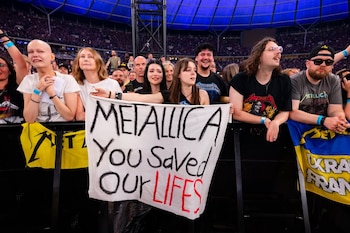 Vista frontal de un grupo de fans en un concierto, algunos llorando, sosteniendo una pancarta que dice 'METALLICA You Saved Our LIVES' en inglés