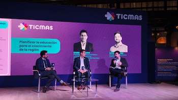 Tres hombres en un escenario durante una presentación. Detrás, una pantalla muestra el logo de TICMAS, texto sobre educación y fotos de panelistas