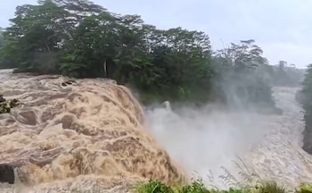 Un río con aguas marrones y turbulentas forma una cascada, con vegetación verde frondosa en los márgenes y neblina de agua