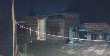 Una casilla de madera y ladrillos de noche, delimitada en el frente por una cinta de seguridad roja y blanca