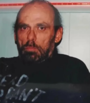 Retrato de un hombre con cabello escaso, barba de varios días y camiseta negra con letras blancas