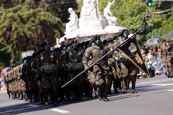 Soldados con uniformes de camuflaje, boinas negras y rostros pintados de verde y negro marchan en una calle, uno sostiene una bandera de Cobras