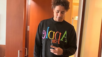 Guillermo Ochoa viste una sudadera negra con letras de colores mientras sostiene un teléfono móvil frente a un espejo.