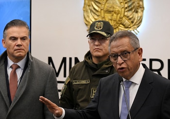 Un hombre con anteojos habla por un micrófono junto a Marco Antonio Oviedo y un oficial uniformado frente a un escudo nacional