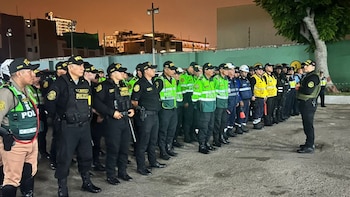 Vista nocturna de un numeroso grupo de policías, serenos y personal de otras entidades en formación al aire libre. Un oficial se dirige a ellos