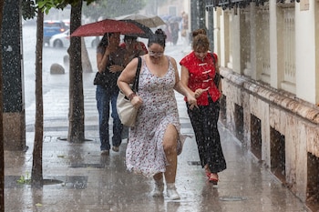 Varias jóvenes corren bajo la intensa lluvia que ha caído este viernes en Murcia. (Marcial Guillén/EFE)