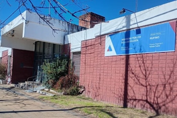 Edificio de la Unidad Fiscal Rufino con paredes de ladrillo rojizo y sección superior blanca. Un cartel azul indica "Ministerio Público de la Acusación"