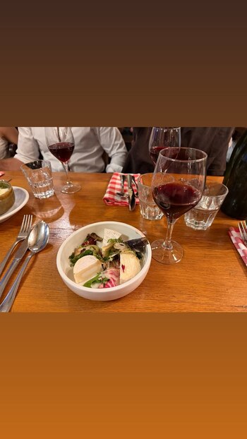 Mesa de madera, un plato hondo con ensalada de hojas verdes y queso, copas de vino tinto, vasos, cubiertos, botella y mantel de cuadros
