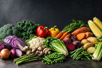Diversas verduras como brócoli, col morada, pimientos, zanahorias, lechuga, patatas y maíz dispuestas sobre una mesa oscura