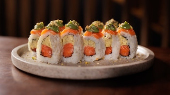 Ocho piezas de sushi con salmón, arroz, relleno cremoso y una salsa verde encima, servidas sobre un plato circular de cerámica