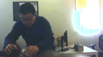 Un hombre con anteojos y abrigo oscuro manipula un frasco pequeño frente a un escritorio con un monitor y un equipo electrónico