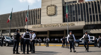 Grupo de policías uniformados con chalecos frente a la entrada de la Alcaldía Venustiano Carranza, con banderas mexicanas y vehículos policiales.