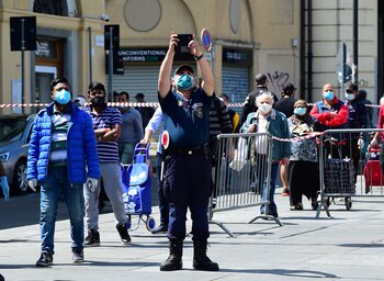Un oficial de policía con una máscara protectora toma una foto en el mercado de Porta Palazzo en Turín después de que reabrió con reglas de distanciamiento social este, 4 de mayo de 2020. (REUTERS / Massimo Pinca)