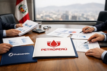 Manos de ejecutivos analizando gráficos y documentos sobre una mesa de madera con logos de Petroperú y Proinversión, con bandera peruana y Lima difusa de fondo.