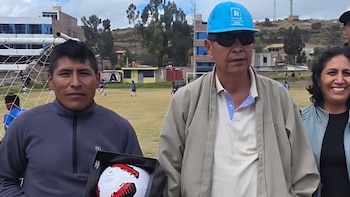 Un hombre con gorra celeste y gafas oscuras posa junto a un hombre que sostiene una pelota de fútbol en caja y a una mujer
