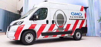 Furgoneta blanca con franjas rojas, el logotipo de GMO, letras en japonés y la silueta del contorno de la cabeza de un robot