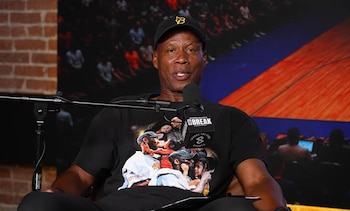 Byron Scott habla frente a un micrófono con una gorra negra y una camiseta estampada
