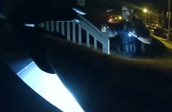 Un agente de policía con una linterna encendida permanece junto a la barandilla de una escalera exterior durante la noche