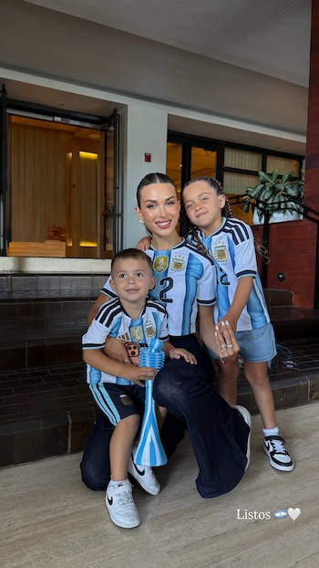 Una mujer, una niña y un niño posan sonrientes, todos vestidos con camisetas de la selección argentina, en el interior de un edificio con escaleras