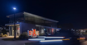 Moderno edificio del Centro de Bienvenida de Arkansas State University iluminado de noche. Se ve el letrero "STATE", farolas y estelas de luz de vehículos en la carretera