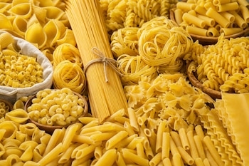 Variedad de pasta seca de distintas formas que incluye espaguetis, lazos, plumas, nidos y láminas de lasaña.