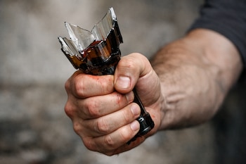 Primer plano de la mano de un hombre que empuña una botella de vidrio rota, con sangre en los nudillos y en el cristal.