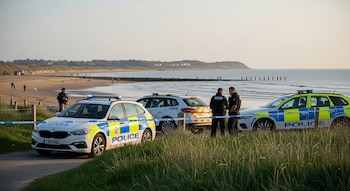 Tres vehículos de la policía de Essex y tres agentes junto a un cordón de seguridad azul y blanco en la entrada de la playa de West Mersea.