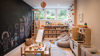 Habitación infantil con una pared de pizarra con dibujos, un rocódromo interior, estanterías de juguetes, un tobogán de madera y una cocinita.