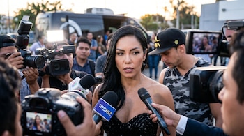 Paloma Fiuza, una mujer de cabello oscuro, es entrevistada por varios reporteros que sostienen micrófonos y cámaras frente a ella en un entorno exterior.