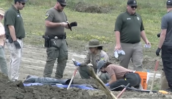Grupo de agentes uniformados y civiles en un terreno de tierra. Se observa una lona azul, herramientas de excavación y vegetación escasa